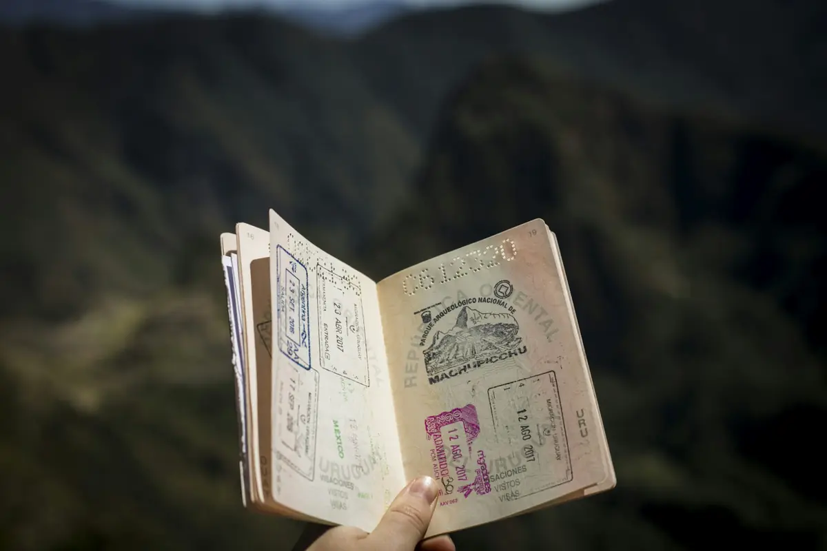 A hand holding an open passport full of stamps